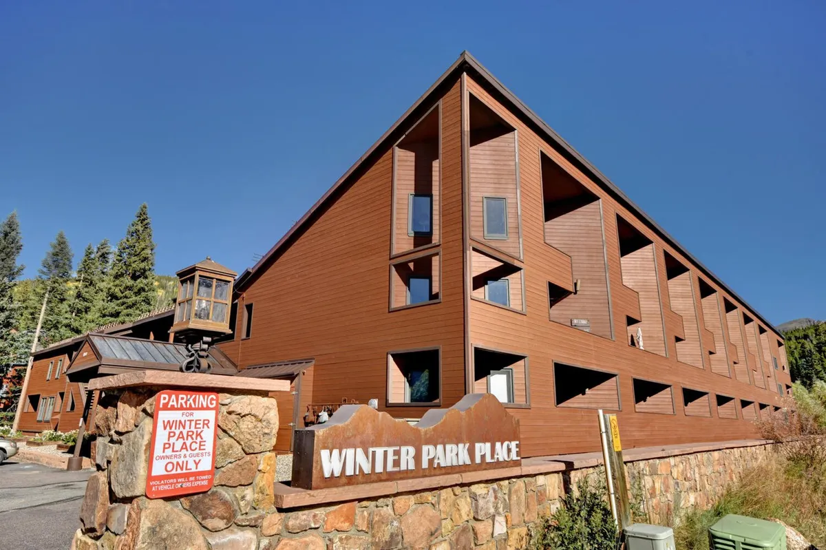 The welcoming facade of Winter Park Place with its sign visible, nestled among trees, offering a sense of arrival and community. The setting feels serene and inviting, suggesting both relaxation and easy access to local amenities.
