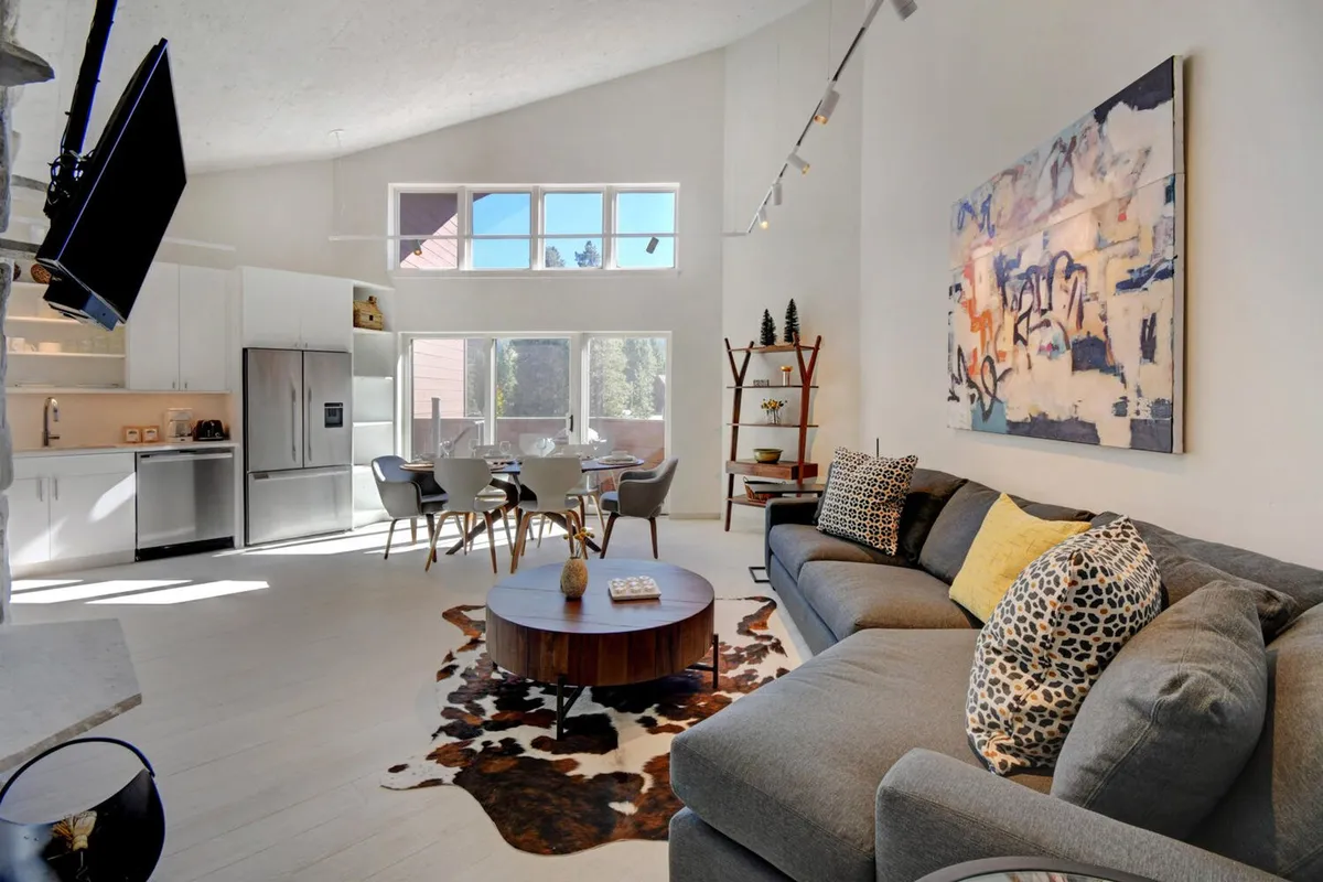 A stylish, contemporary living and dining area featuring a plush modern sofa, a striking abstract painting as the centerpiece, and a sunlit dining table set—inviting spaces perfect for relaxing or gathering with loved ones.