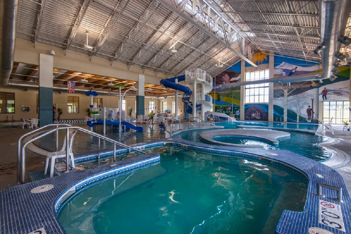 A vibrant indoor recreation center filled with children playing on water slides, a swimming pool, and colorful mural artwork. The space is lively, capturing the fun of year-round recreation.