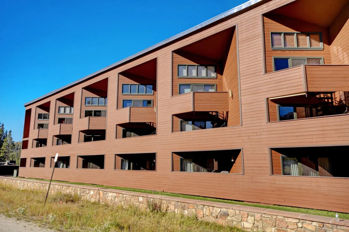 A welcoming exterior shot showcasing a wooden building with large windows and balconies overlooking the surrounding nature. The atmosphere is cozy, suggesting both relaxation and appreciation of the outdoors from the comfort of the property.