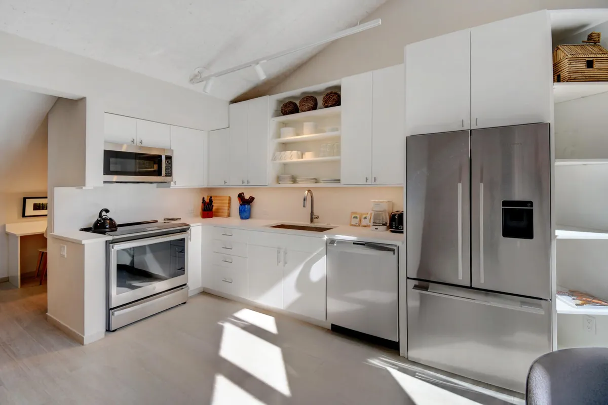 This image showcases a modern kitchen with sleek stainless steel appliances, open shelving displaying dishes, and a large window that bathes the space in natural light. The setting feels contemporary and inviting, ideal for cooking, entertaining, and family gatherings.