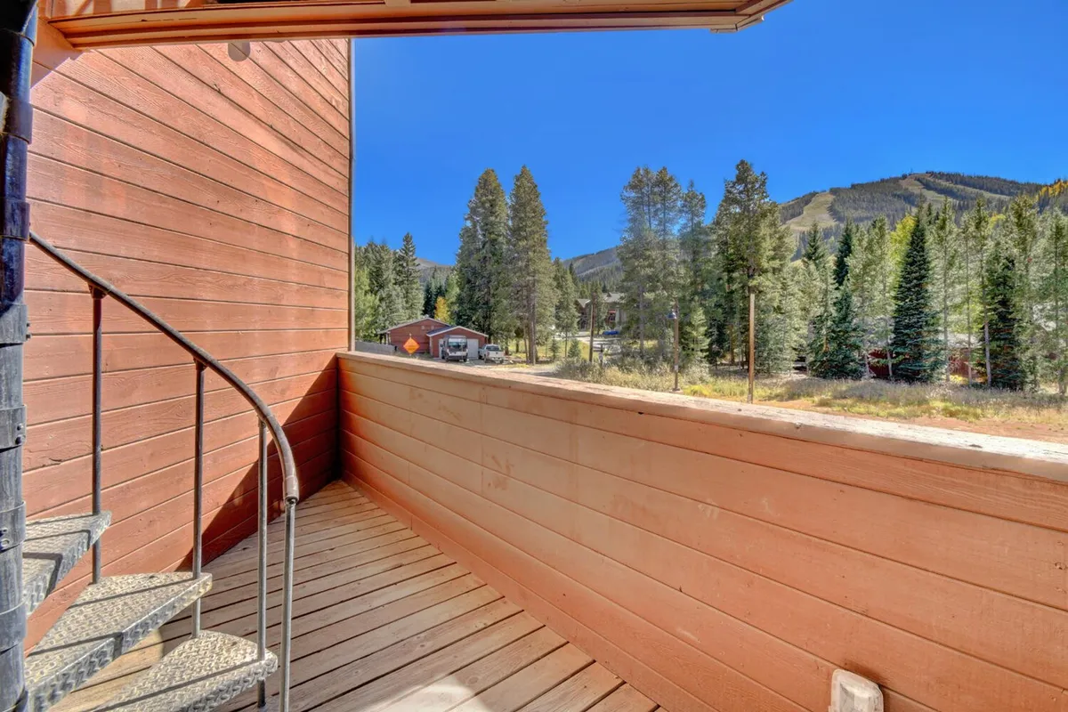 A tranquil exterior setting featuring a spiral staircase with a wooden railing, set against a stunning mountain backdrop and framed by surrounding trees. The space is ideal for relaxation, morning coffee, or enjoying breathtaking sunset views.