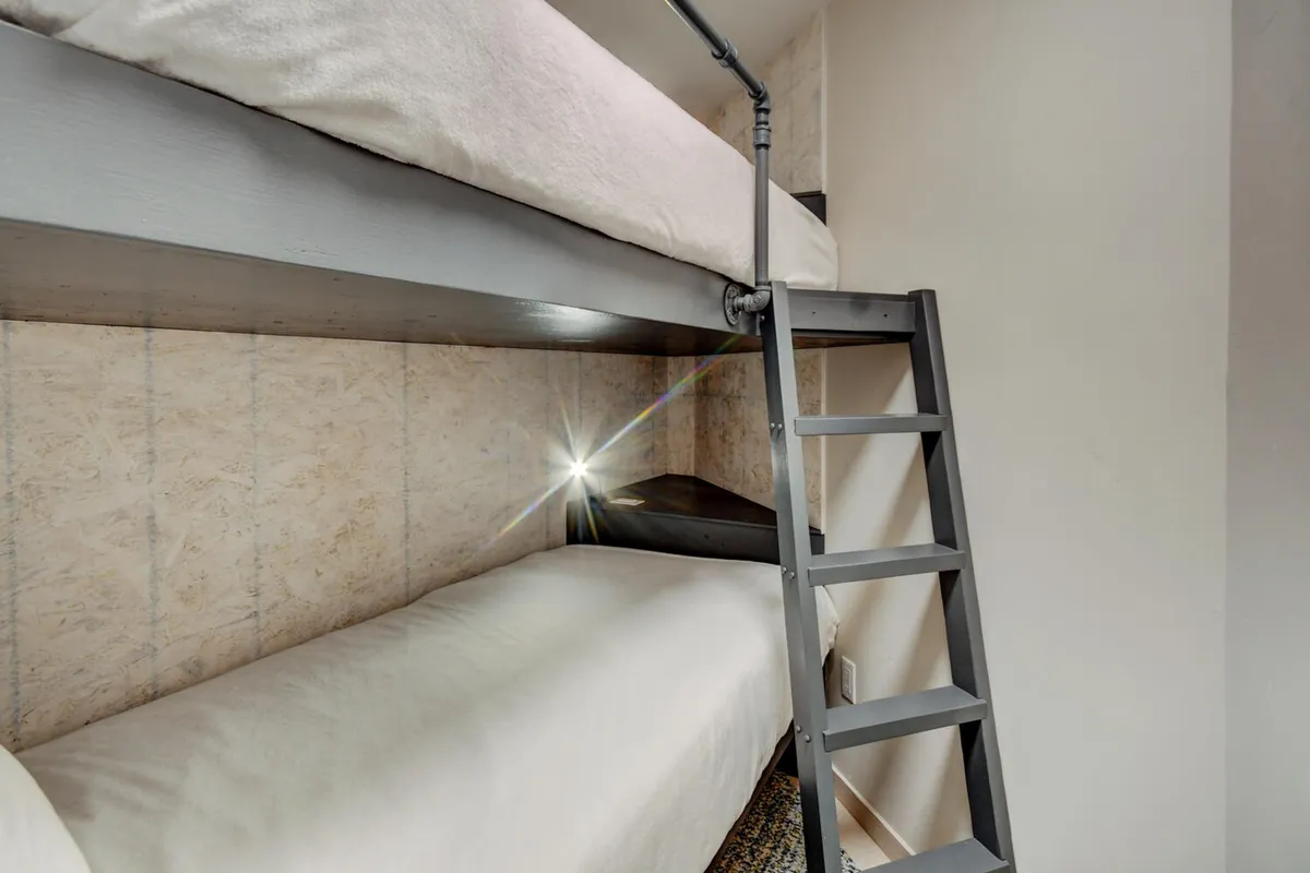 A cozy corner in a bedroom showcasing twin bunk beds with a sturdy ladder and soft wall lighting, perfect for family or kids’ accommodations. The arrangement is intimate, ideal for late-night storytelling and group stays.